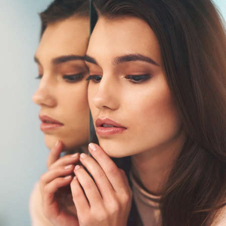 The mirror does not define your beauty. Shot of a beautiful young woman leaning against a mirror.の写真素材