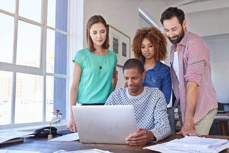 He needs their input. Cropped shot of three young designers gathered around a laptop in the...