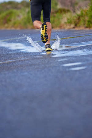 Hit the road - whatever the weather. Cropped image of a runners legs as he runs onwards.