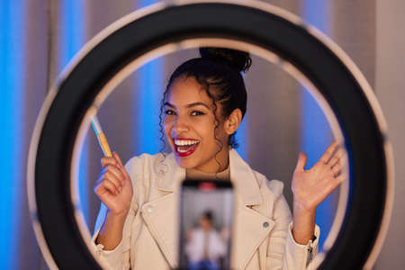 This is the final look. Shot of a young woman using a phone and ring light to film a makeup tutorial...