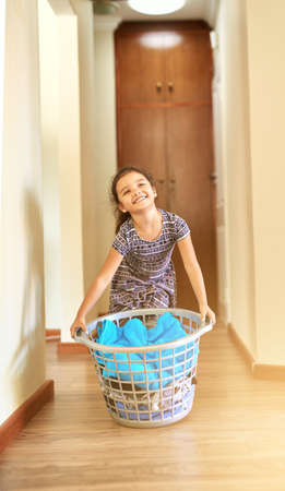 Shes a big help around the house. Shot of a young girl holding a basket of laundry.の写真素材