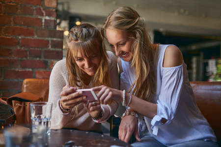 Open that. Cropped shot of two attractive young girlfriends looking at a cellphone while sitting in...