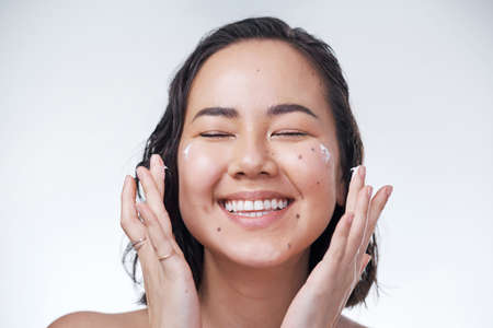 Our skin needs a little extra TLC. Cropped shot of a beautiful young woman applying moisturiser to her face.の写真素材
