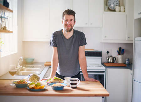 This is my diet for the day. Portrait of a handsome young man standing in front of meals which he has prepared in his kitchen.の写真素材