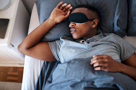 Sleeping in is my favourite pastime. Cropped shot of a handsome young man wearing a night mask and...