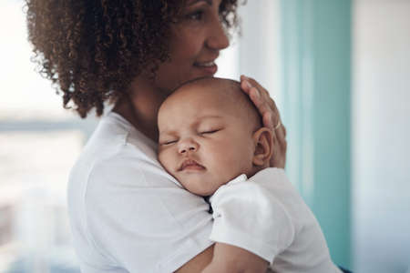 Shh, mommy is here. Shot of an adorable baby girl sleeping peacefully in her mothers arms at home.