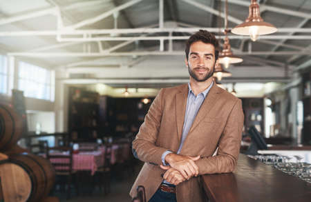 They serve my favourite beer here. Cropped portrait of a handsome young man standing in a bar.の写真素材