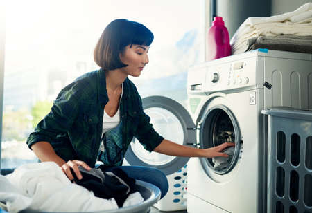 Making sure I sort the colors properly. Shot of a young woman doing her laundry at home.の写真素材