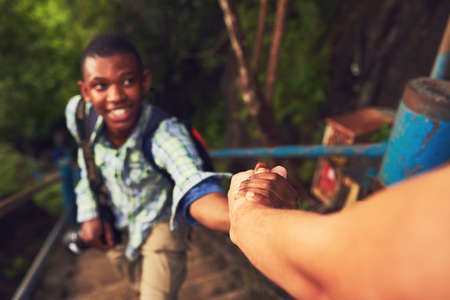 Its no challenge if we do it together. Cropped shot of a young man helping a friend up a mountain...