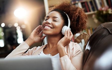 Thats some smooth sound. Shot of a young woman relaxing on the sofa and listening to music on her laptop.の写真素材