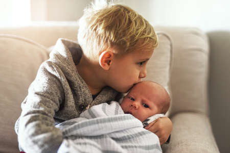 Too much cuteness. Shot of a cheerful little boy holding his little infant brother and giving him a...