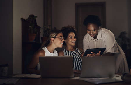 Some of the biggest successes are built in the dark. Shot of a group of young businesswomen using a laptop and digital tablet during a late night at work.の写真素材