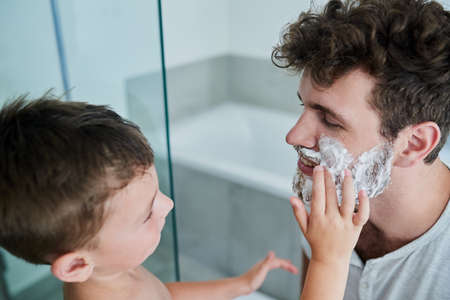 Let me do it for you Dad. Shot of a little boy rubbing shaving cream on his fathers face in the bathroom at home.の写真素材