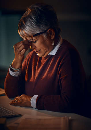 It might be time to call it a night. Shot of a mature businesswoman looking stressed out while working late in an office.の写真素材