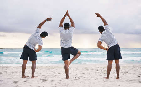 Tripling his fitness. Rearview shot of three unrecognizable male athletes practicing yoga on the...