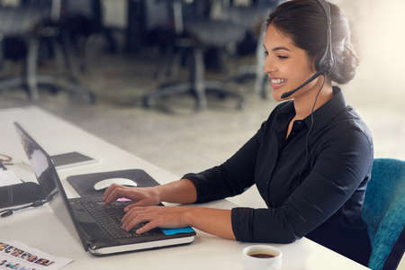 Pleased to be of assistance. Shot of a call centre agent sitting at her desk in a modern office.