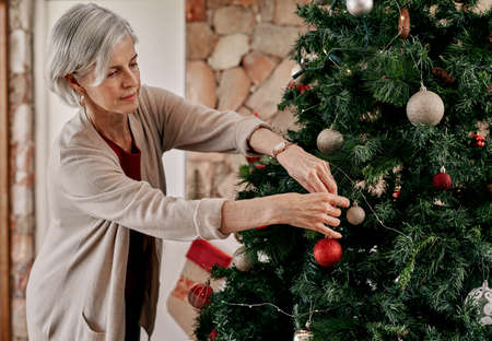 You can go right here. Cropped shot of a carefree mature woman placing decorations on a Christmas tree inside at home during the day.の写真素材