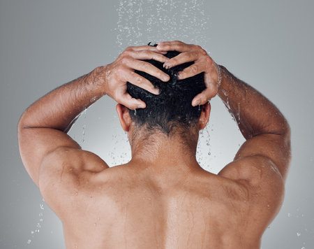 Time for a relaxing shower. Shot of an unrecognizable man washing his hair in the shower against a grey background.の写真素材