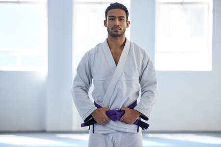 Im almost at the top. Cropped portrait of a handsome young male martial artist standing with his hands on his belt in the gym.の写真素材