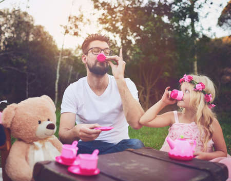 This tea is great. Shot of a cheerful daughter and father having a tea party with a bunch of stuffed toys in the middle of a garden.の写真素材