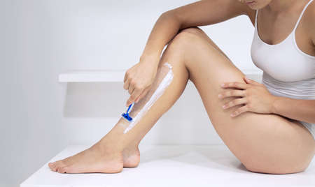 Smooth legs are the way to go. Cropped shot of an unrecognizable woman sitting down and shaving her legs at home.の写真素材