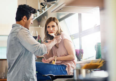 Tell me what you think.... Shot of a young man giving his wife a taste of the meal hes preparing.の写真素材