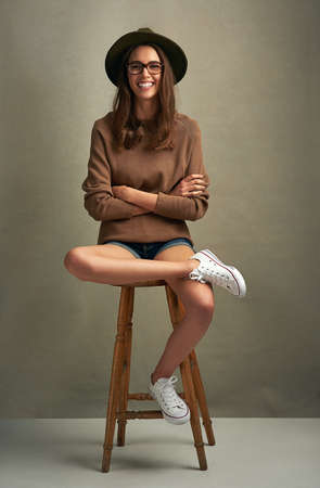 Individuality is the definition of freedom. Shot of a beautiful young woman sitting against a brown background.の写真素材