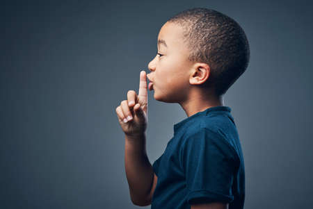 I can keep a secret if you can. Studio shot of a cute little boy posing with his finger on his lips...