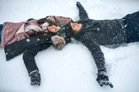 The snow make us feel like kids again. High angle shot of a couple lying in the snow making snow angels.の写真素材