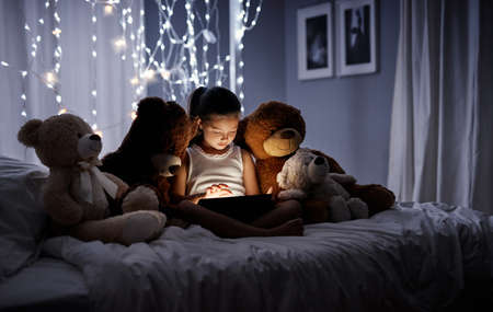 Introducing her teddies to technology. Shot of an adorable little girl using a digital tablet in bed at night.の写真素材