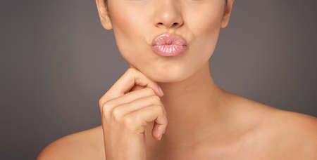 Pucker and pout. Closeup studio shot of a woman with gorgeous glossy lips against a gray background.の写真素材