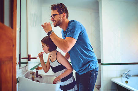 Keeping those pearly whites very bright. Shot of a father and his little daughter brushing their...