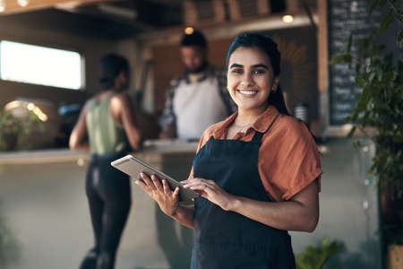 Lets get you seated. Shot of an attractive young woman standing outside her restaurant and using a digital tablet.の写真素材