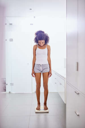Now thats what I like to see. Shot of an attractive young woman weighing herself on a scale in the bathroom at home.の写真素材