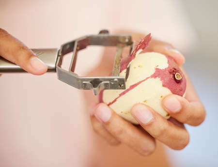 Shot of a woman peeling a potato in her kitchen.の写真素材