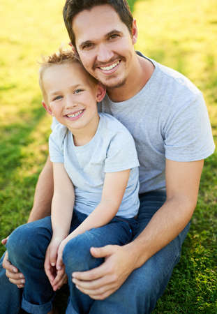 Smiles and sunshine in the park. Portrait of a smiling father and his little son sitting on the...