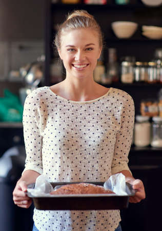 Healthy homemade bread- you should try some. Portrait of a young woman holding a freshly baked bread loaf in a pan.の写真素材