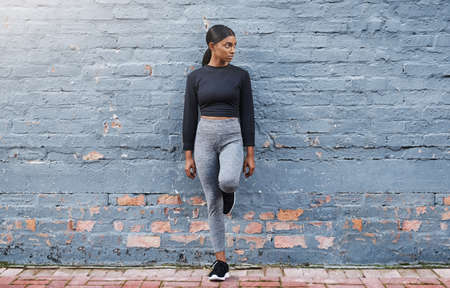 Dressed for fitness success. Shot of a fit young woman leaning against a gray wall outdoors.の写真素材