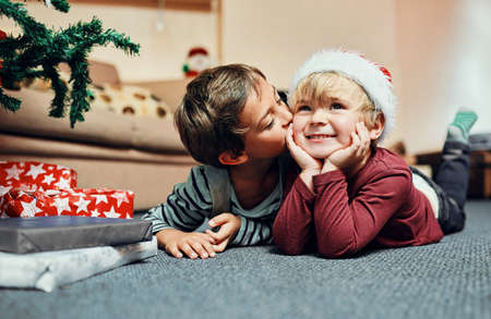 Santas gift this year No sibling rivalry. Shot of an adorable little boy giving his brother a kiss while waiting to open their Christmas presents.の写真素材