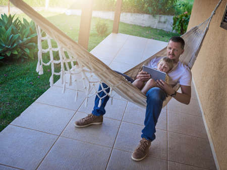 Its their comfy spot to get connected. Shot of a father and his little daughter using a digital tablet while relaxing on a hammock outdoors.の写真素材