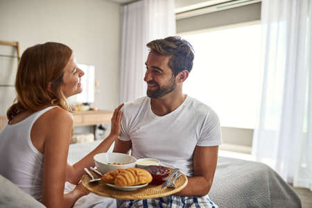 Romance is, breakfast in bed. Shot of a happy young couple enjoying breakfast in bed together at home.の写真素材