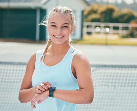 I always time myself to my first point. Shot of an attractive young woman standing alone and checking her watch during tennis practise.の写真素材