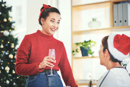 Were feeling merry and festive today. Shot of two attractive young women drinking champagne and celebrating together at their office Christmas party.の写真素材