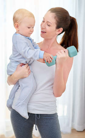 Youre going to be a strong young man. Shot of a young woman working out while spending time with her baby boy.の写真素材