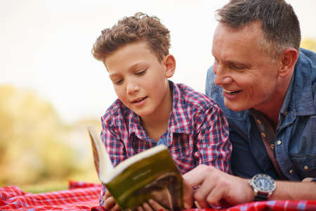 Books are gifts you can open again and again. Shot of a father and son reading a book together in a park.の写真素材