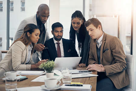 The strategy experts. Shot of a group of young businesspeople using a laptop together during a meeting in a modern office.の写真素材