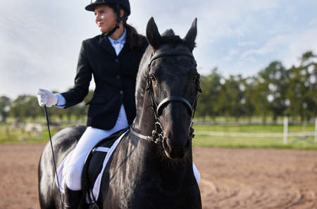 Training on horseback. Cropped shot an attractive young female jockey riding her horse out on the farm.の写真素材