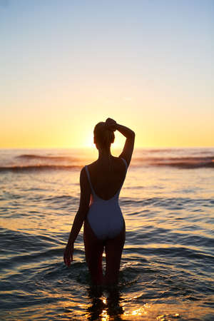 We all get lost in the beauty sometimes. Rearview shot of a young woman standing in the water at...