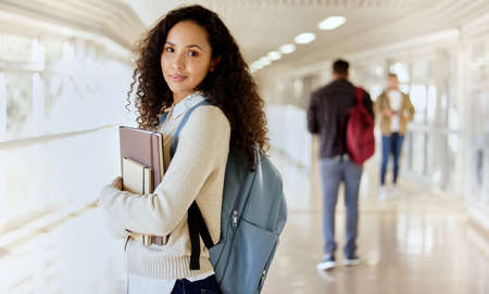 Im off to class. Cropped portrait of an attractive young female college student standing with her textbooks in a campus hallway.の写真素材