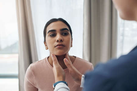 This area can become quite an irritation during sickness. Shot of an unrecognizable doctor feeling a patients throat in an office.の写真素材